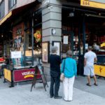 Three people standing outside a corner store with vibrant displays.