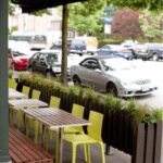 Outdoor seating with wooden tables and yellow chairs along a street.