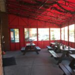 Outdoor dining area with picnic tables under a red canopy.