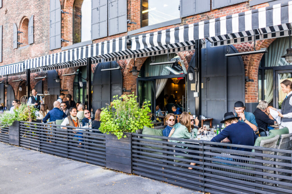 People dining outdoors at a busy restaurant with striped awnings.